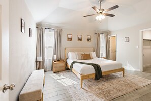 A bedroom with a bed, nightstands, a bench, a ceiling fan, and a door.