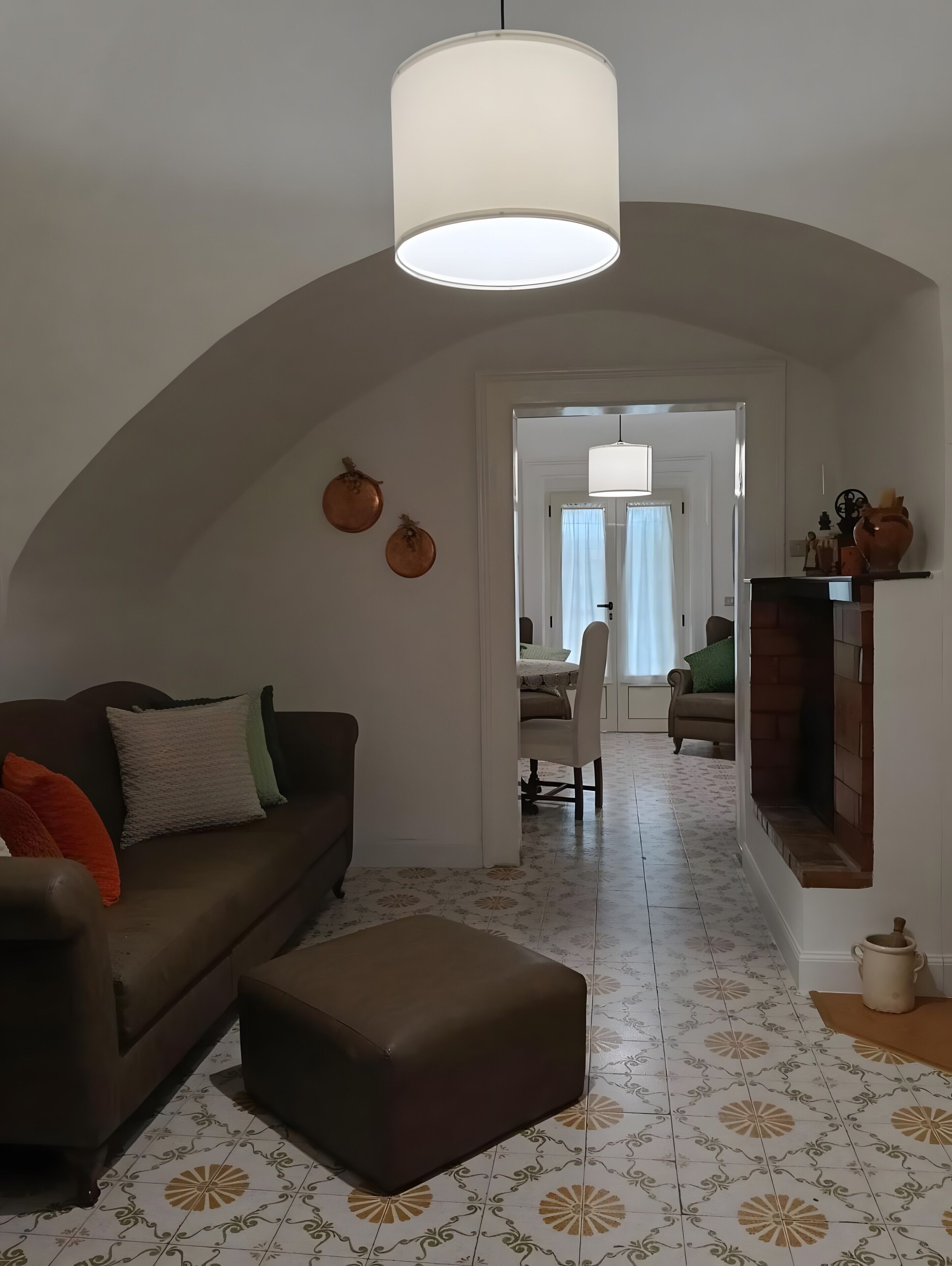 Uma sala de estar com sofá, banquinho e luminária pendente.