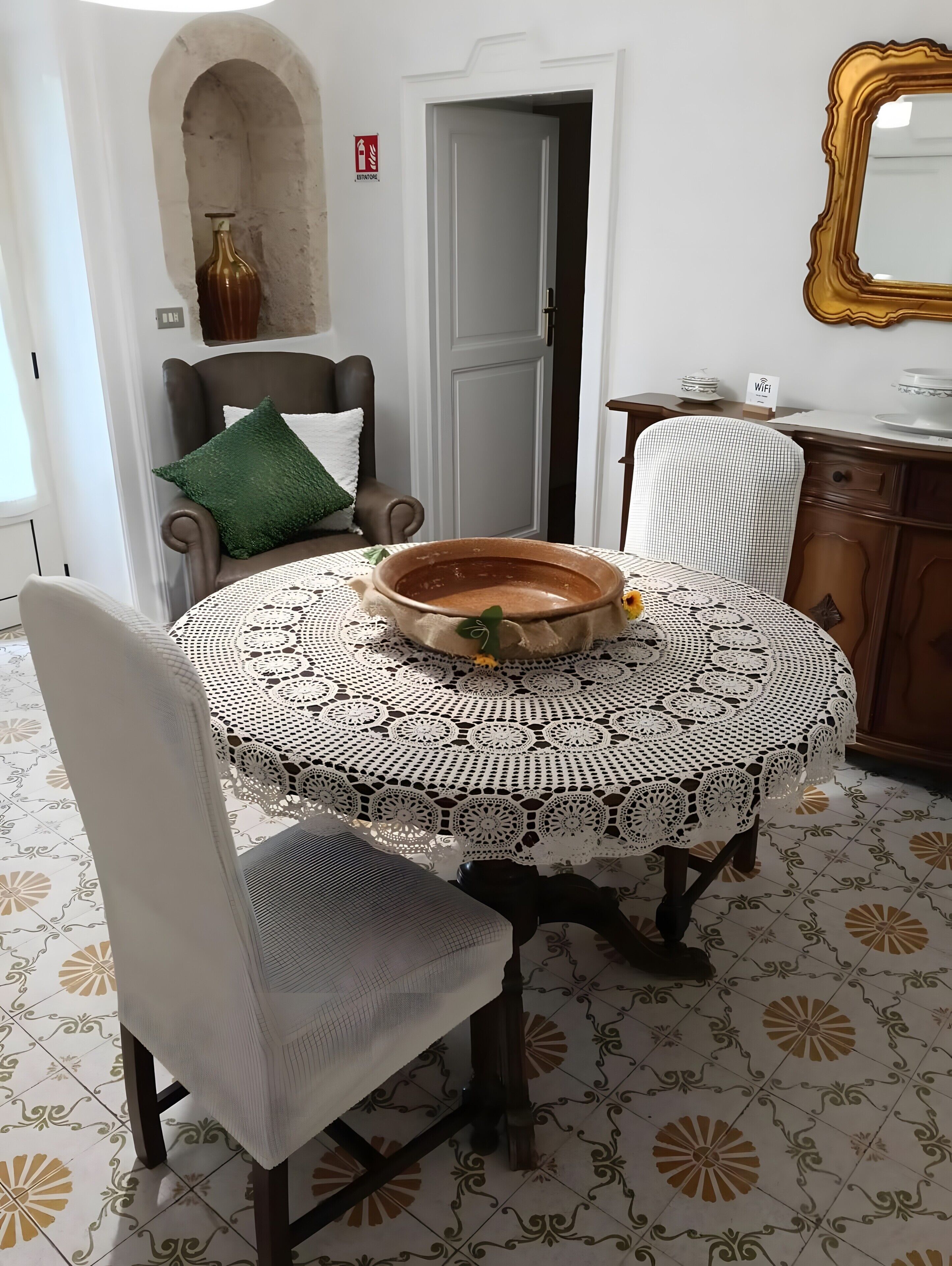 A dining area with a round table, two chairs, a decorative bowl, a vase, and a door with a fire exit sign.