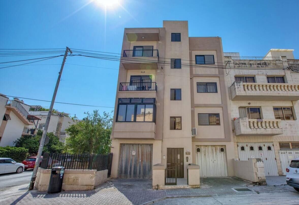 Un immeuble résidentiel à plusieurs étages, doté de balcons, d’une entrée sécurisée et surplombant un ciel dégagé.