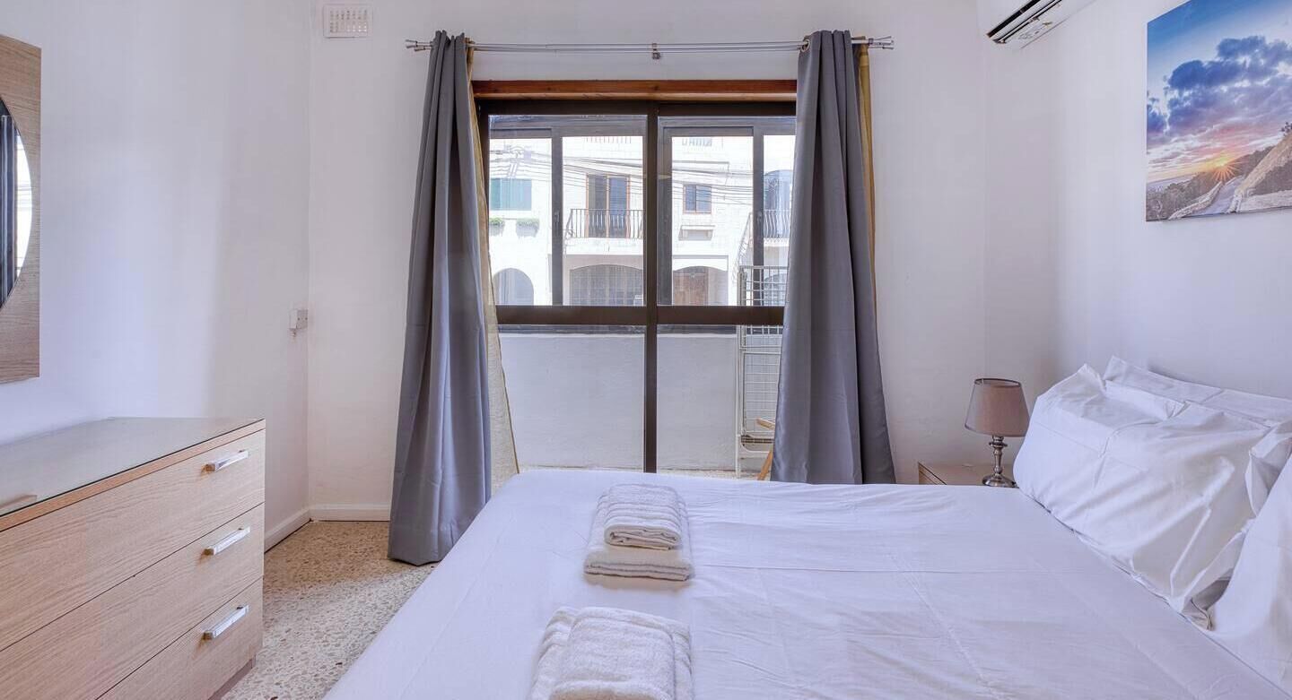 Ein Hotelzimmer mit Bett, Schminktisch, Fenster mit Vorhängen und einem Bild an der Wand.