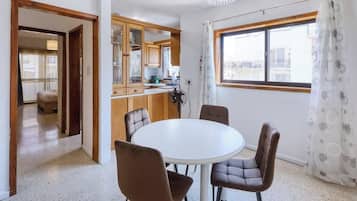 A compact kitchen with wooden cabinets, a dining table with four chairs, and a window with a view of buildings.