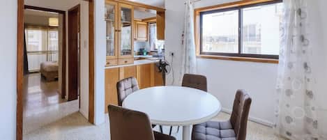 A compact kitchen with wooden cabinets, a dining table with four chairs, and a window with a view of buildings.