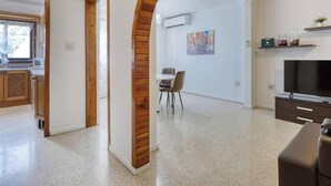 A modern living room with a flat-screen TV, a dining area with chairs, and a kitchen with wooden cabinets. - Beautiful 2BR Apartment in Swieqi with Balcony (Swieqi)
