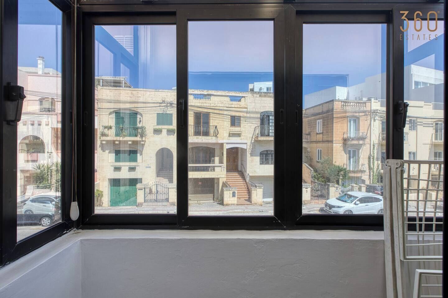A window with a view of a residential area, including buildings and a street.