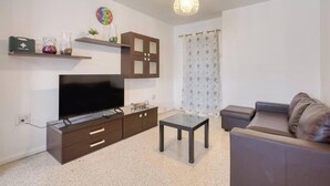 A living room with a flat-screen TV, a sofa, a coffee table, a cabinet, and a shelf with decorative items. - Beautiful 2BR Apartment in Swieqi with Balcony (Swieqi)