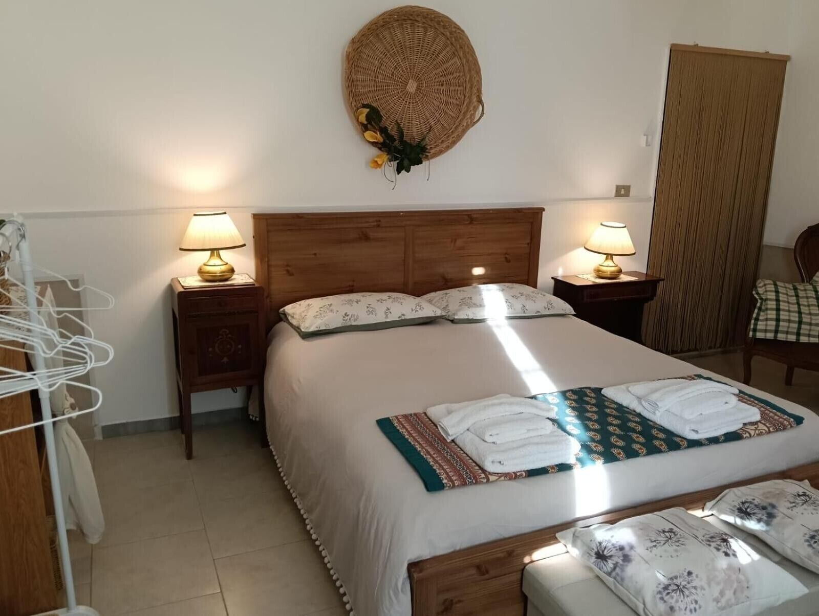 A hotel room with a large bed, two bedside tables with lamps, a wooden headboard, and a woven wall hanging.
