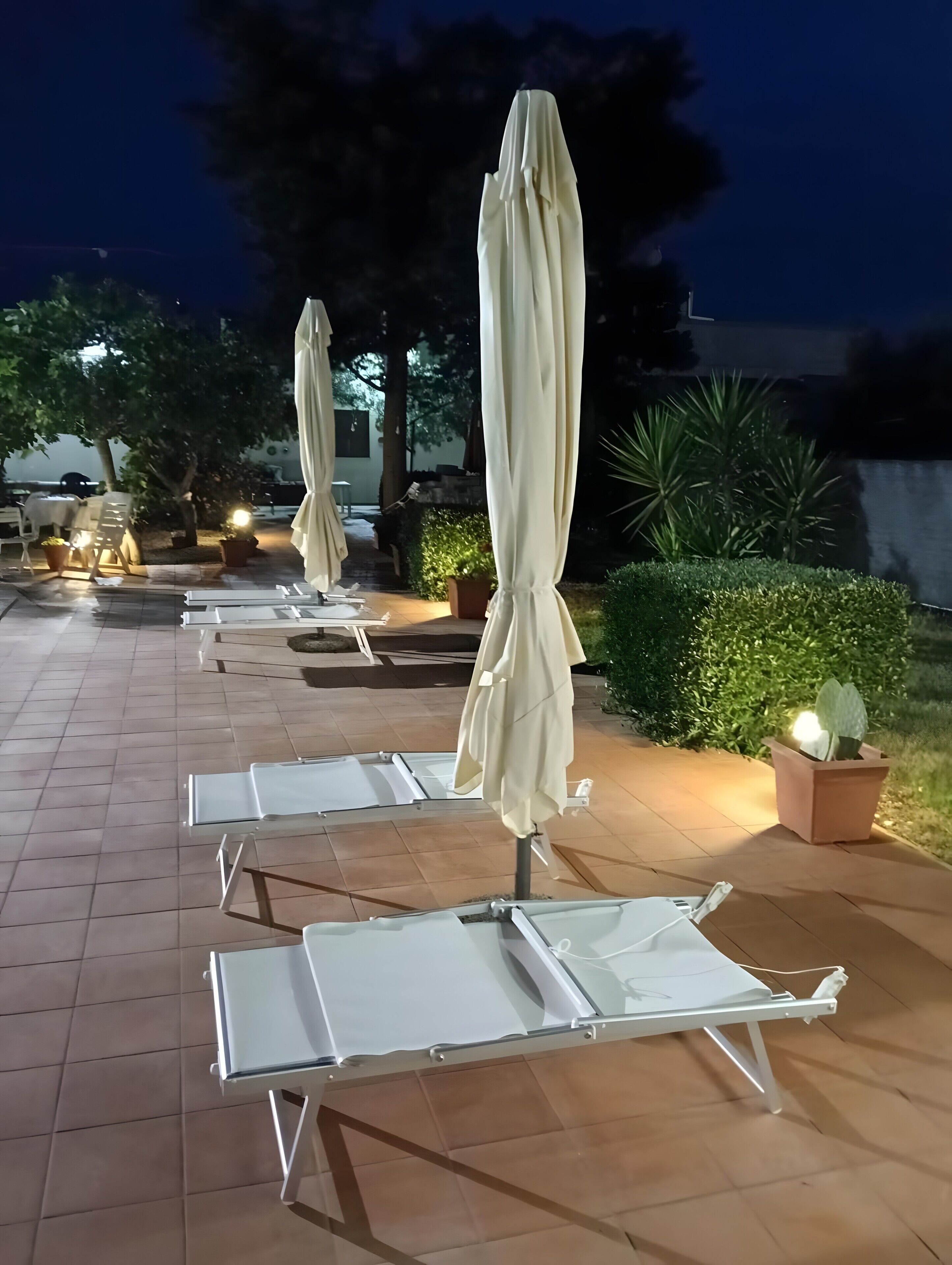 Outdoor lounge chairs and umbrellas arranged on a tiled patio.