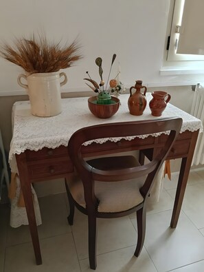 A dining table with a lace tablecloth, a wooden chair with a cushioned seat, and a vase with dried plants.