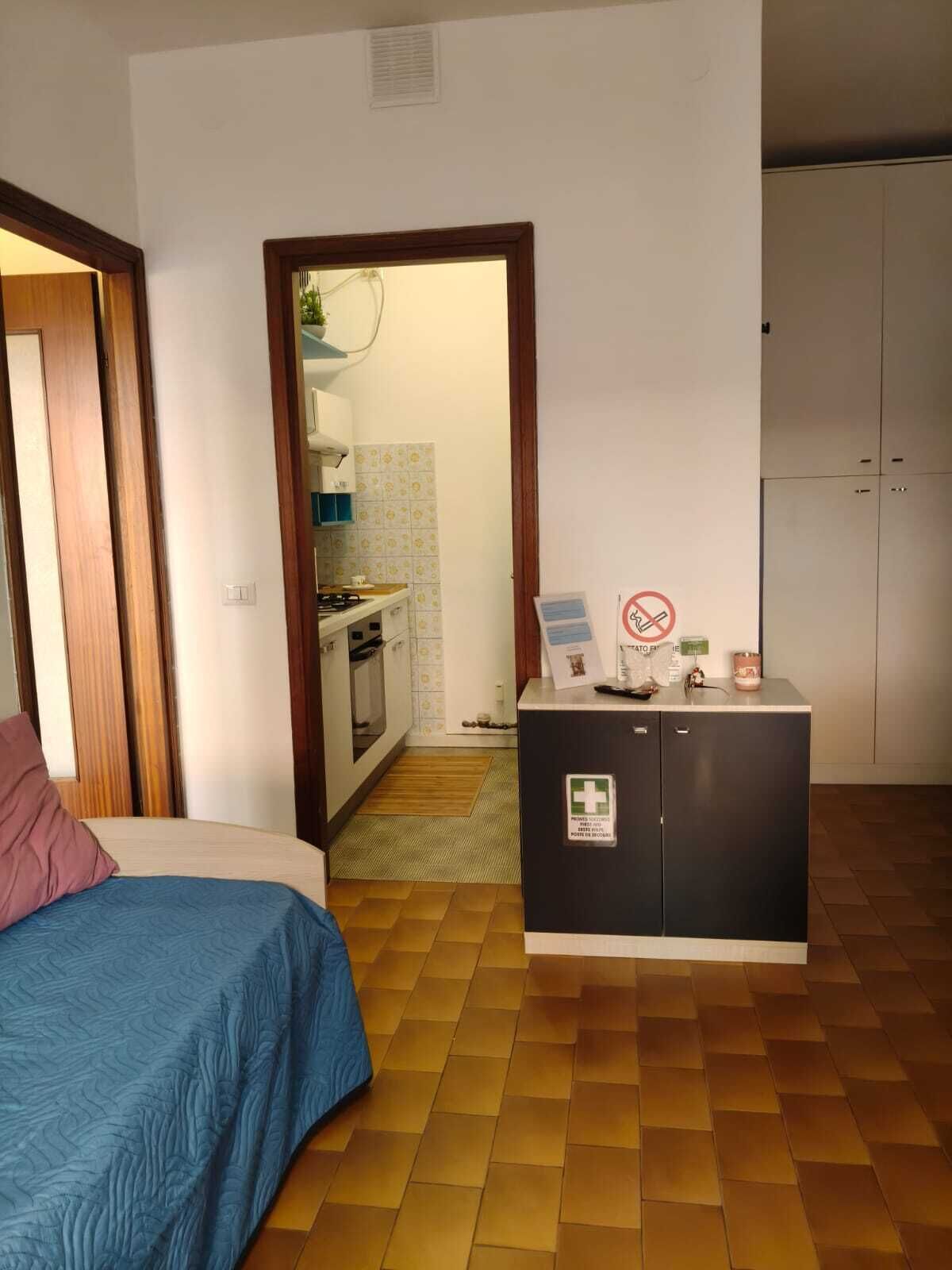 Hotellihuone, jossa on sänky, pieni keittiö, ensiaputarvikkeita sisältävä kaappi ja vaatekaappi.
