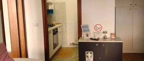 A hotel room with a bed, a kitchenette, a cabinet with a first aid sign, and a wardrobe.