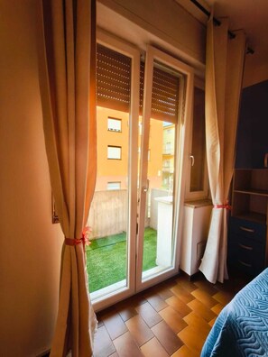 Ein Zimmer mit einer Schiebetür zu einem Balkon mit einem grünen Rasen, einem Bett mit blauen Kissen und einem Holzboden.