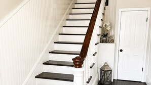 Eine Treppe mit weißen Geländern und dunklen Stufen, die zu einer weißen Tür mit einem 'hello' Schild führt.