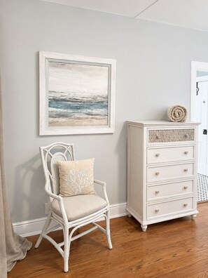 A room with a white wicker chair, a white dresser with drawers, and a framed artwork on the wall. - Uptown 2nd story APT - blocks from the fort! (St. Augustine)