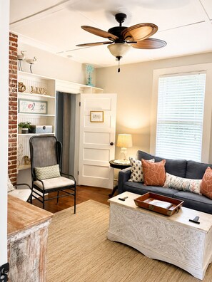 Un salon doté d’un ventilateur de plafond, d’un canapé agrémenté de coussins à motifs, d’une table d’appoint avec une lampe et d’un fauteuil décoratif.