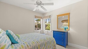 Ein Schlafzimmer mit einem Bett, einem Schminktisch, einem Spiegel und einem Deckenventilator.
