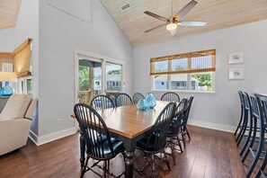 Une salle à manger avec une table et des chaises en bois, un ventilateur de plafond et des fenêtres équipées de stores.