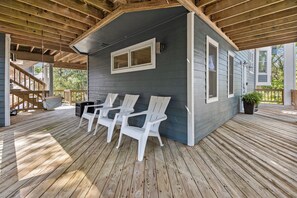 Un espace extérieur abrité, doté d’un sol en bois, de chaises en plastique blanches et d’un petit bâtiment avec des fenêtres.
