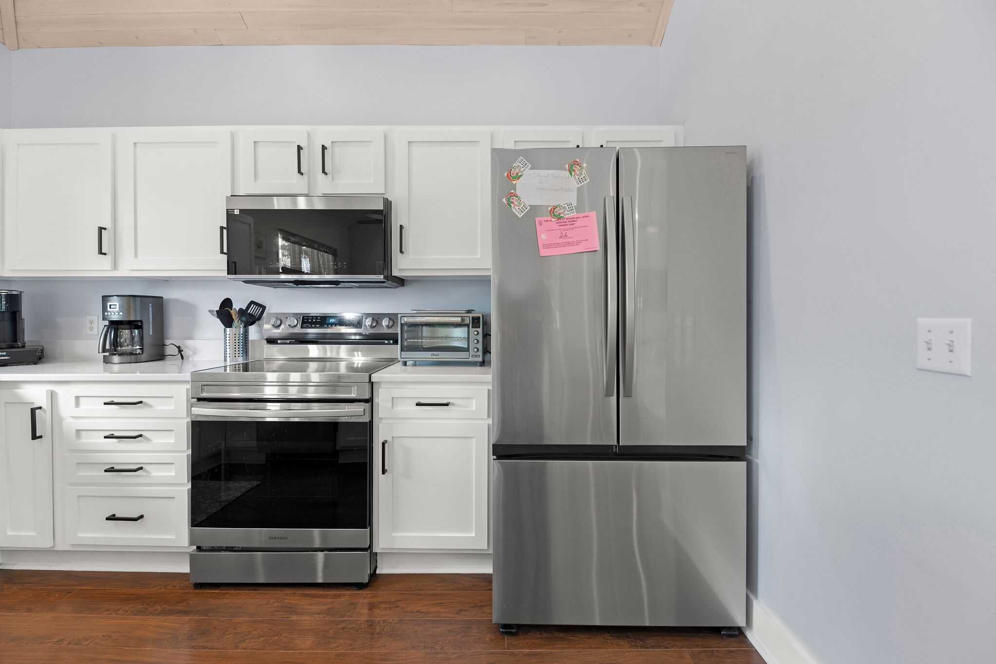 A modern kitchen with white cabinets, stainless steel appliances including a refrigerator, microwave, oven, and coffee maker.