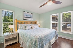 Une chambre à coucher comprenant un lit, une table de chevet, un ventilateur de plafond et des fenêtres équipées de stores.