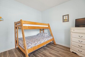 Ein Stockbett mit gemustertem Lattenrost, eine Kommode mit Schubladen und ein gerahmtes Bild an der Wand.