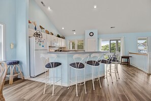 A kitchen with a central island, bar stools, a refrigerator, and a microwave. - I'm Lov'n Sea and Sand: Dog Friendly | 4Br (Corolla)