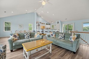 A spacious living room with a large sectional sofa, a wooden coffee table, and a dining area with a kitchen in the background. - I'm Lov'n Sea and Sand: Dog Friendly | 4Br (Corolla)