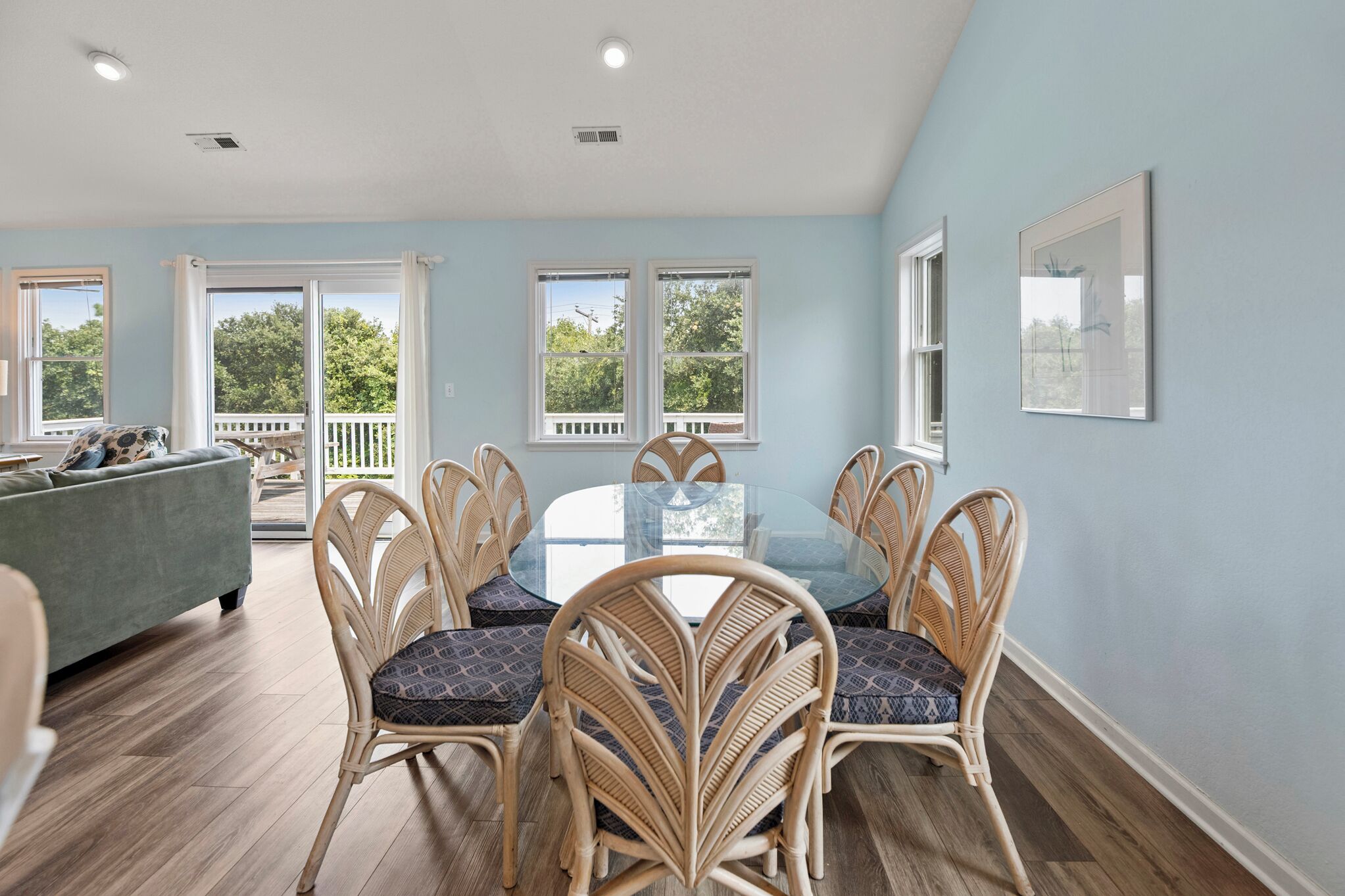 A dining area with a round table and wicker chairs, a pool, and a view of trees through large windows.