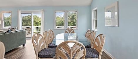 A dining area with a round table and wicker chairs, a pool, and a view of trees through large windows.