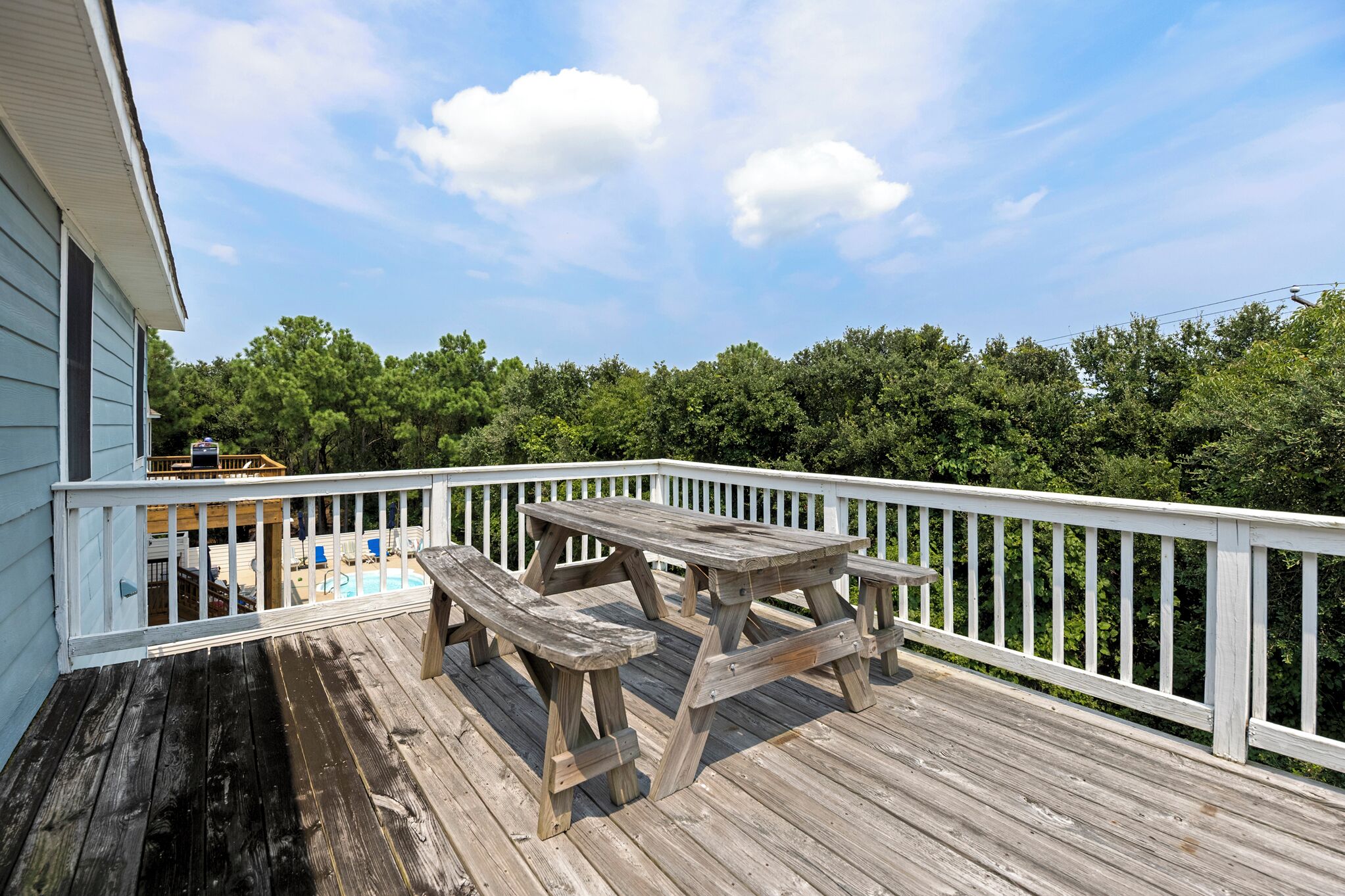 A wooden deck with a picnic table and chairs, surrounded by a white railing.