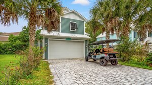 A two-story house with a garage, surrounded by palm trees and a paved driveway. - Green Sandlapper: Golf cart included, North Litchfield Pawleys Island (Pawleys Island)