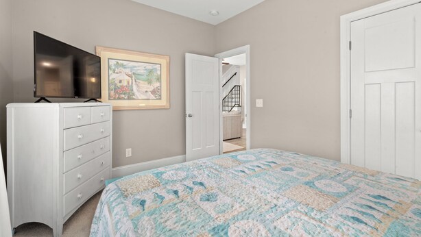 A bedroom with a bed, a dresser, a television, and a door leading to another room. - Green Sandlapper: Golf cart included, North Litchfield Pawleys Island (Pawleys Island)