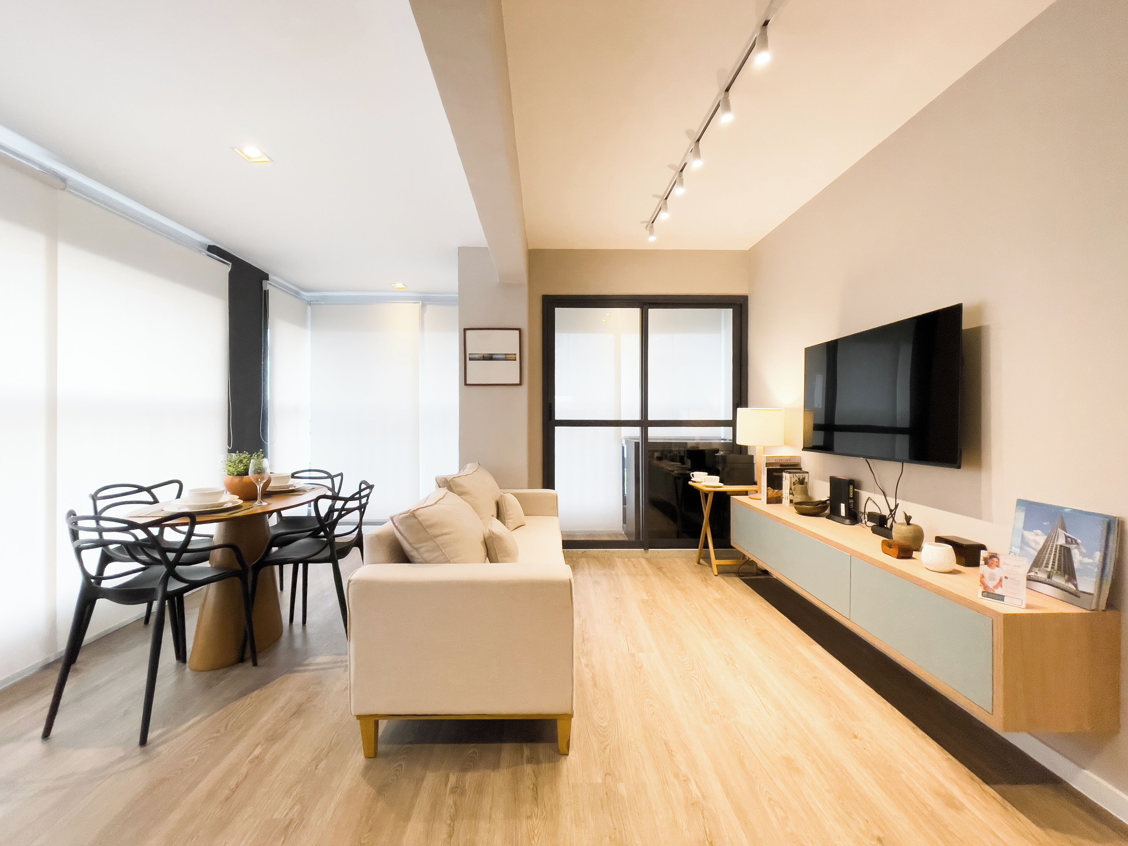 A modern living room with a sofa, dining table, chairs, and a TV mounted on the wall.