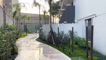 Un sendero que conduce a un edificio de fachada blanca, rodeado de follaje y palmeras.