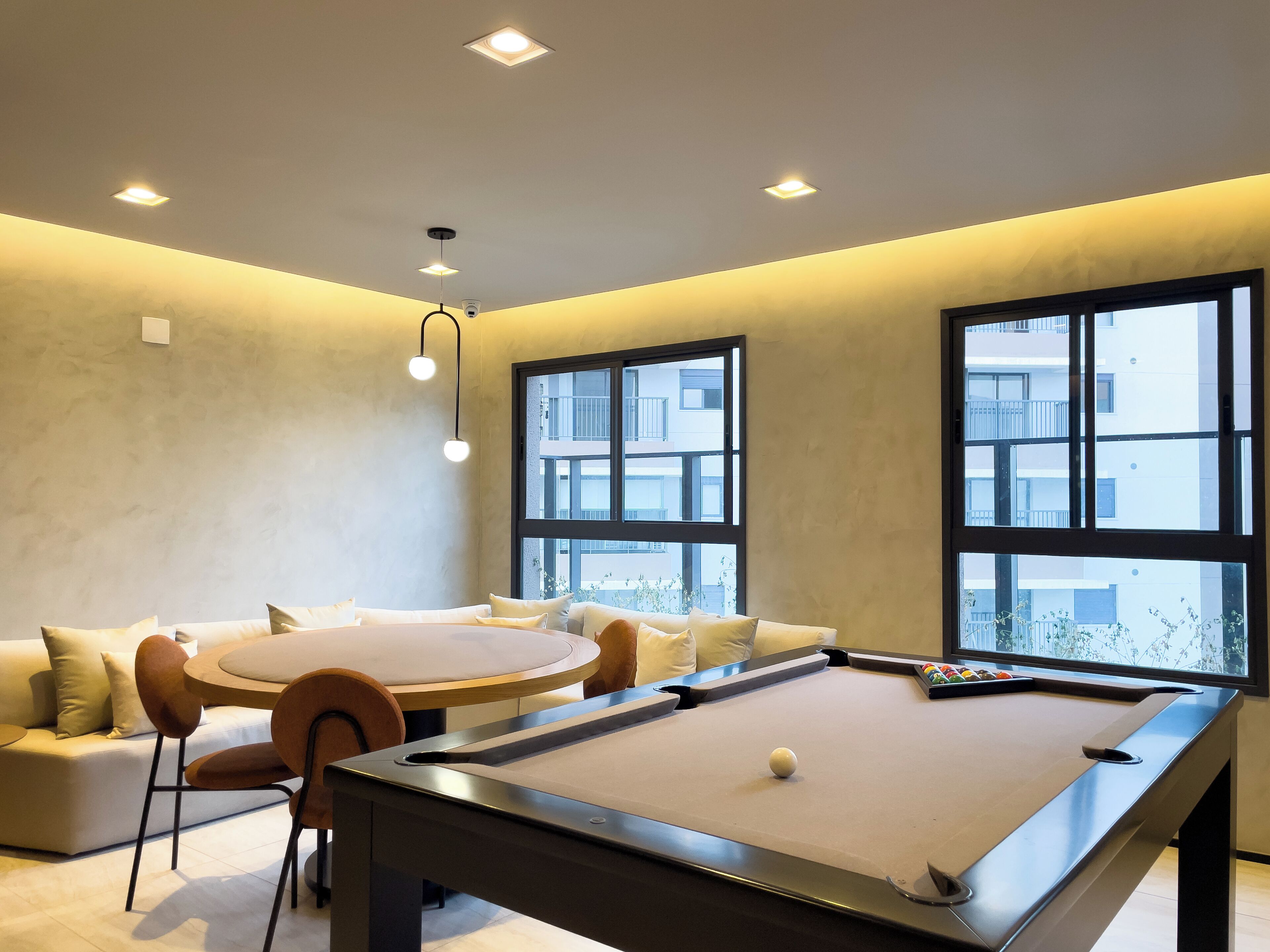 A modern living room with a pool table, a round dining table, and a sofa.