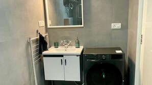 A compact bathroom with a white sink, mirror, and a black washing machine. - Entire rental unit in Bengaluru, India (Bengaluru)