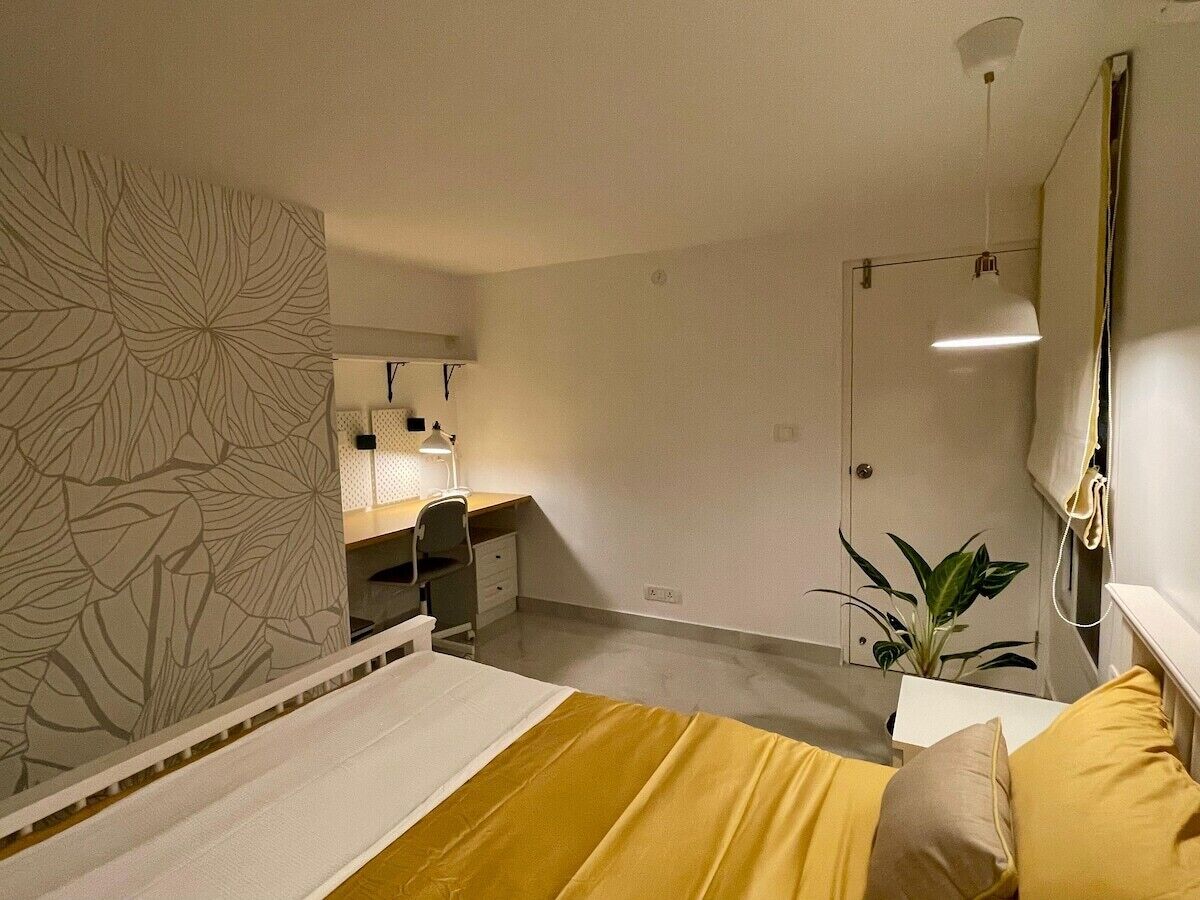 A bedroom with a bed, a desk, and a chair. There is a plant on the desk.