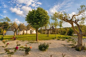 Ein Garten mit verschiedenen Bäumen, ein weißes Gebäude und ein klarer Himmel.