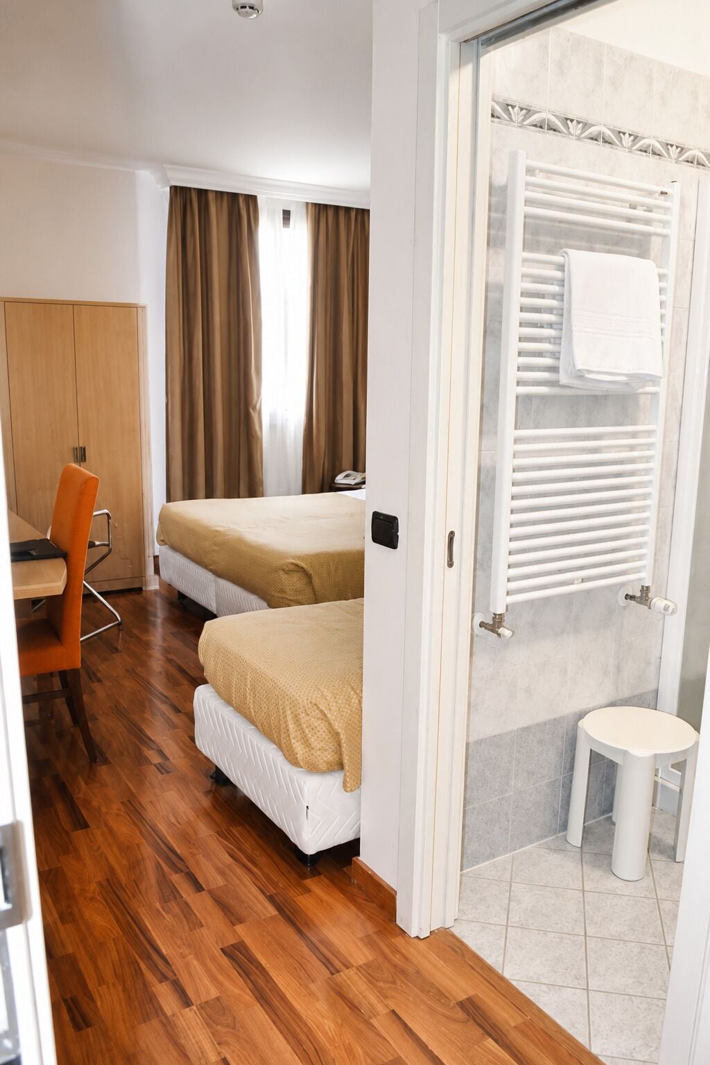 Ein Hotelzimmer mit zwei Betten, einem Schreibtisch, einem Stuhl, einem Badezimmer mit Toilette und Waschbecken sowie einer Dusche.