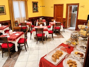A dining area with multiple tables and chairs, a buffet with various food items, and a kitchen area visible through an open door. - Hotiday Reggio Emilia Gaida (Reggio nell'Emilia)
