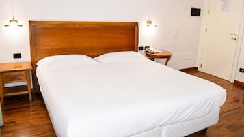 A hotel room with a large bed, wooden headboard, bedside tables, and a painting on the wall.
