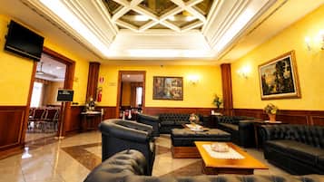 A hotel lobby with a high ceiling, a seating area with sofas and chairs, a television, and a painting on the wall.
