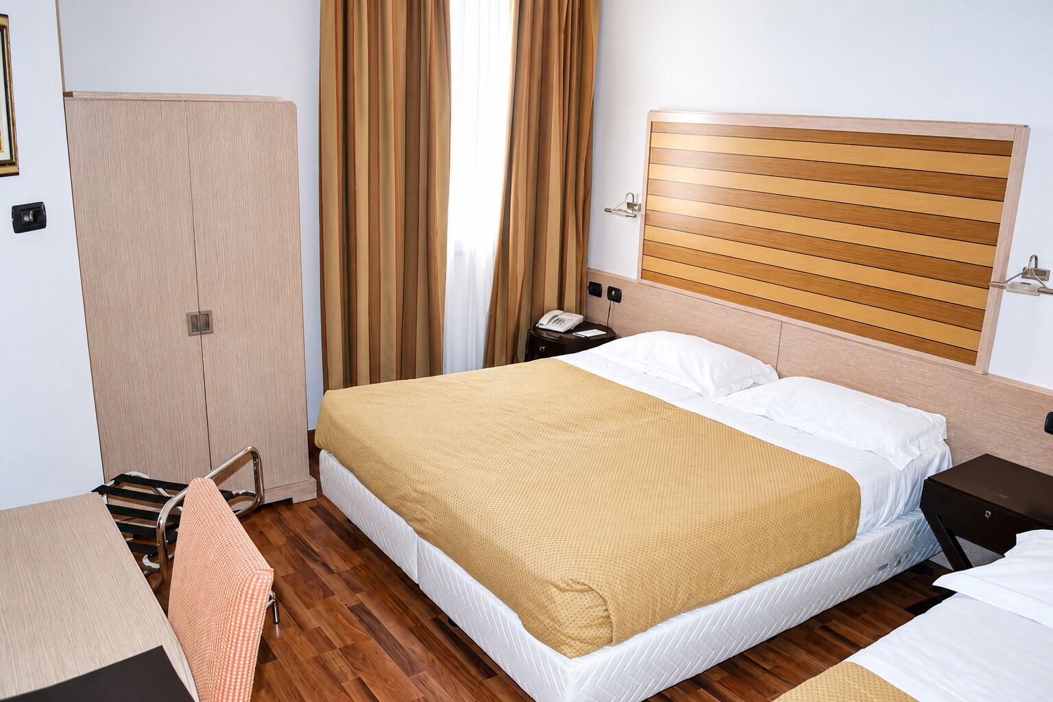 Una camera d'albergo con un letto, un comodino e una scrivania con una sedia.