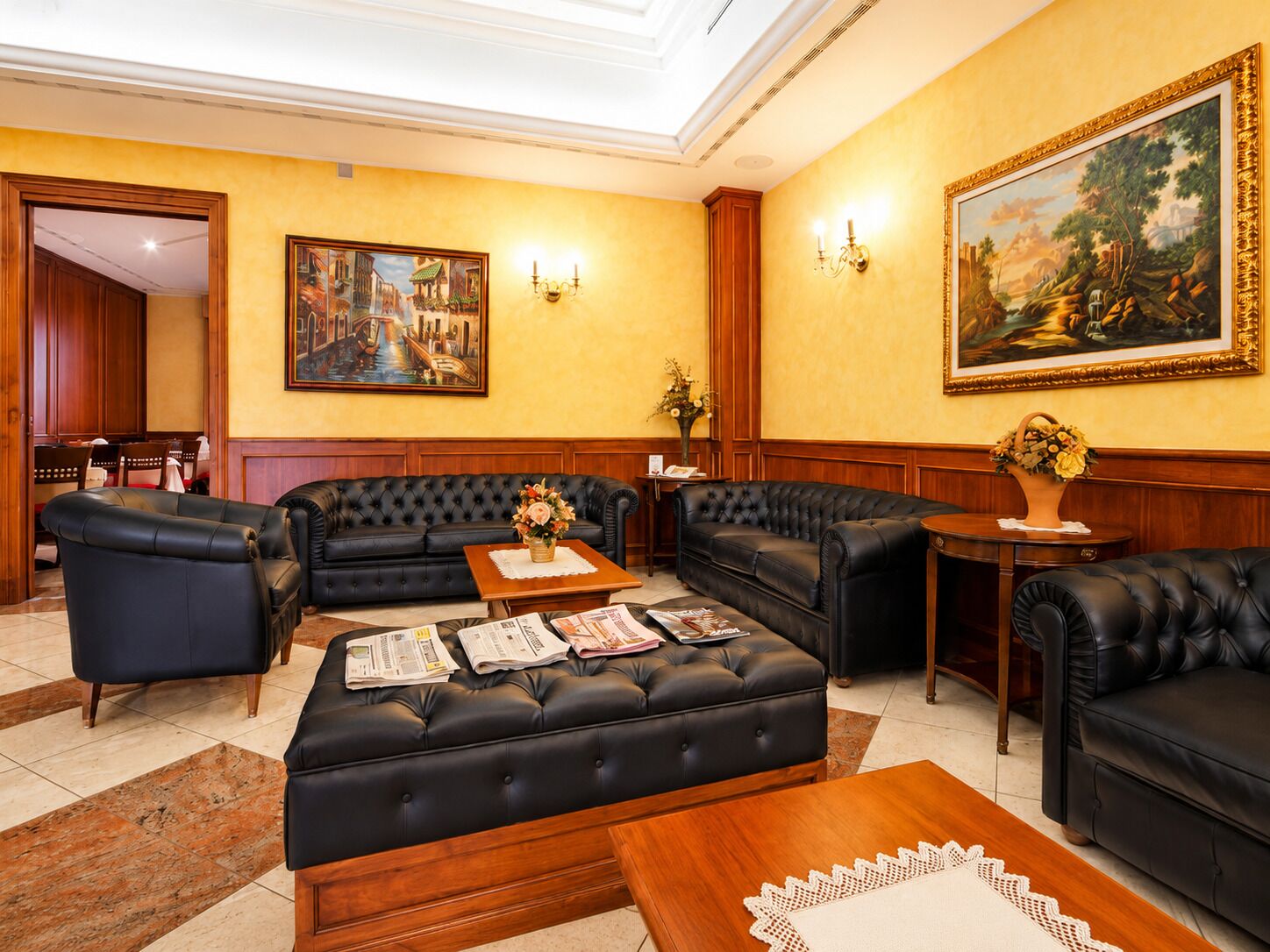 Een hotel lobby met leren banken, een bijzettafeltje met kranten, een schilderij aan de muur en een houten kast.