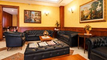 Een hotel lobby met leren banken, een bijzettafeltje met kranten, een schilderij aan de muur en een houten kast.