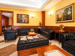 Un vestíbulo de hotel con sofás de cuero, una mesa de centro con periódicos, un cuadro en la pared y un armario de madera.