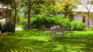 A grassy outdoor area with a table and chairs, surrounded by trees and shrubs.