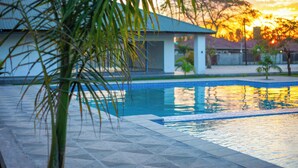 A swimming pool with a tiled deck, surrounded by palm trees and a building with a blue roof.