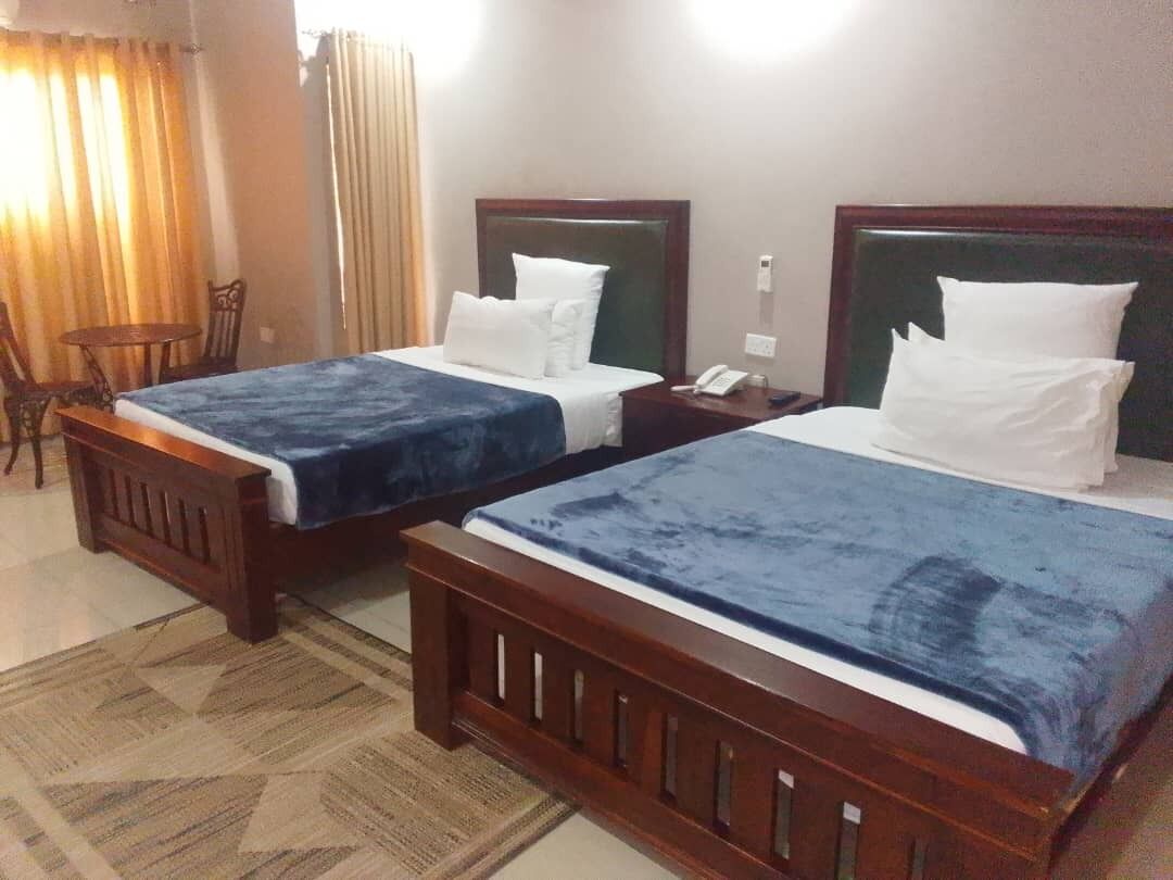 Duas camas de solteiro com cabeceiras de madeira, uma mesinha e uma cadeira em quarto de hotel.