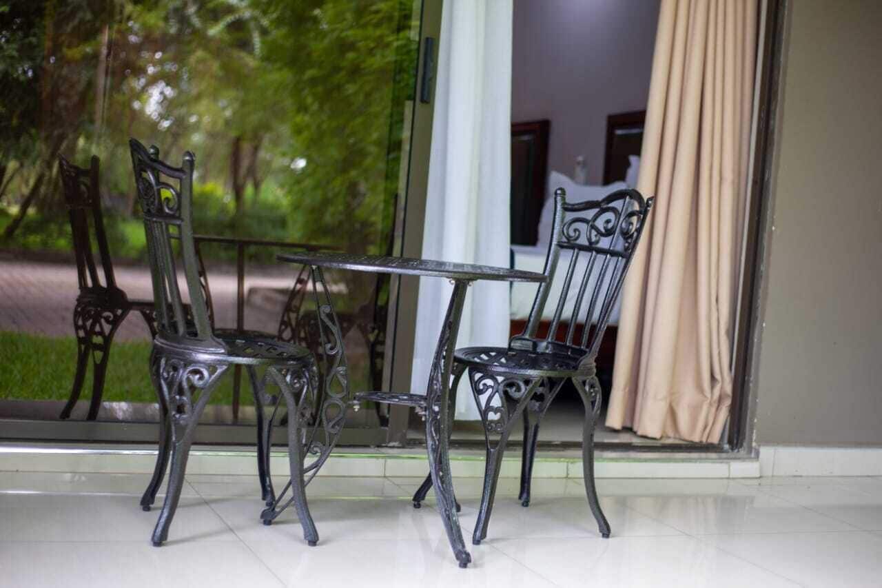A room with a glass door leading to a garden, a table with chairs, and a view of trees outside.